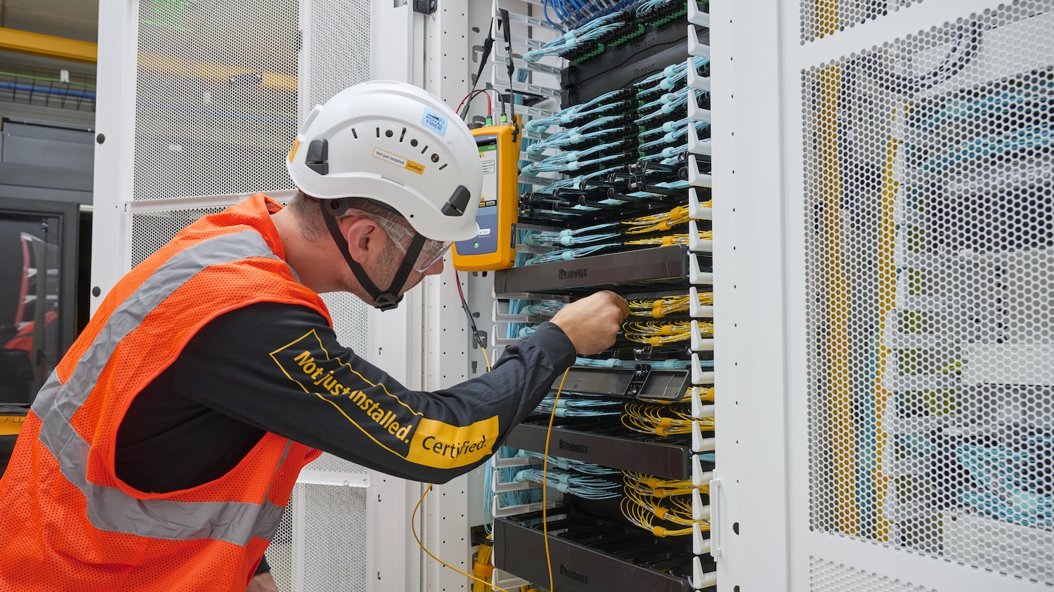 Technician plugging a test cord into a black patch panel in a high-density server rack.