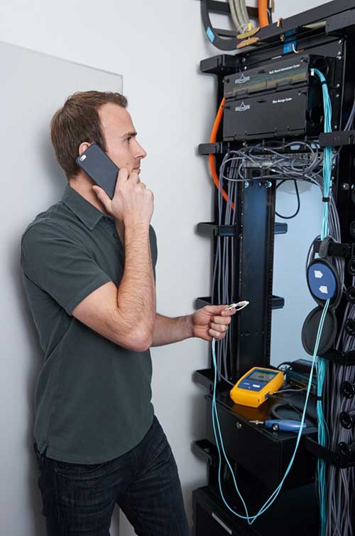 Image of a technician using an OTDR to troubleshoot a fiber link in a telecommunications room